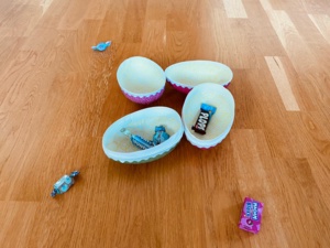 Fyra påskägg i en klunga på golvet. Godis ligger i och runt äggen.